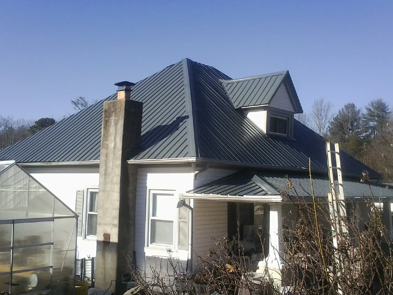 Dark blue standing seam metal roof on a white farmhouse with dormer — Slate & Tile Roof Repair by Roofing Brothers in Sardis